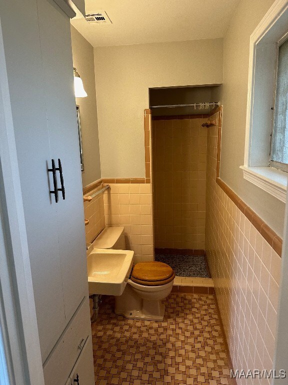 bathroom with sink, toilet, a tile shower, and tile walls