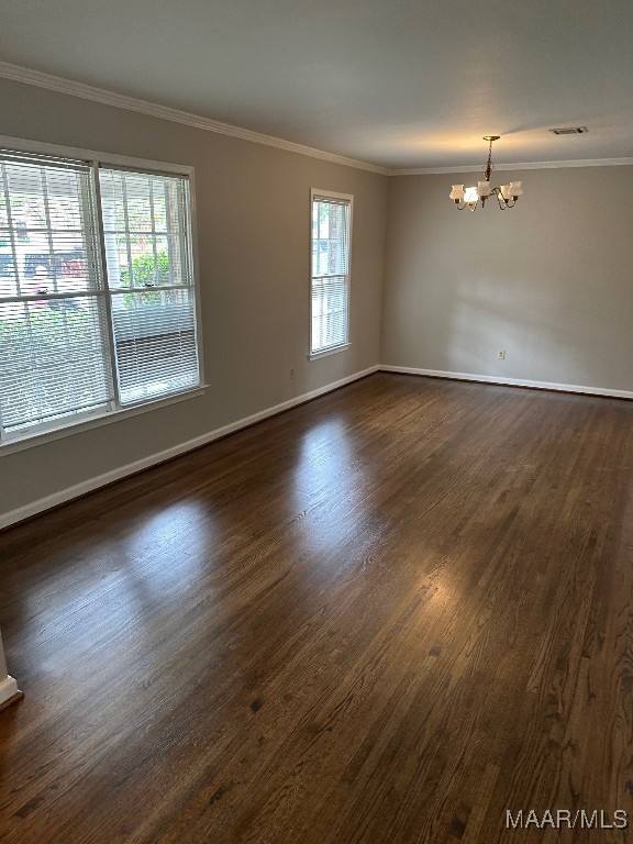 empty room with dark wood-type flooring, an inviting chandelier, and ornamental molding