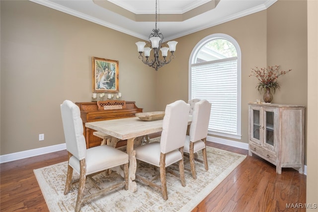 dining area featuring a notable chandelier, a raised ceiling, ornamental molding, and dark wood-type flooring