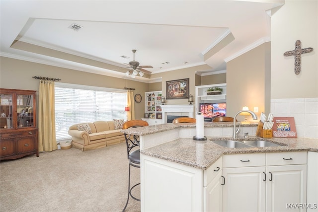 kitchen with light colored carpet, sink, light stone countertops, a kitchen bar, and white cabinetry