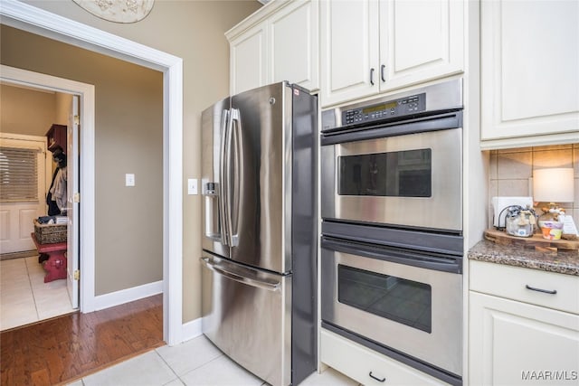 kitchen featuring white cabinetry, stainless steel appliances, backsplash, dark stone counters, and light wood-type flooring