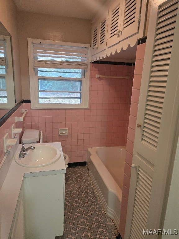 bathroom with tile walls, a bath, vanity, and toilet