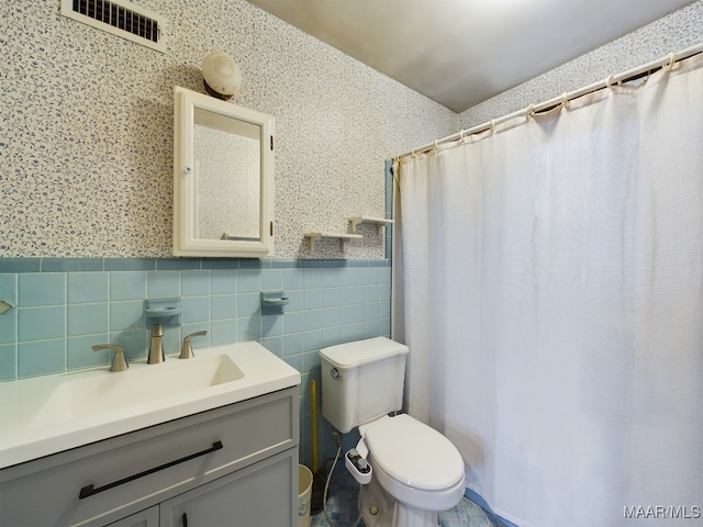 bathroom featuring walk in shower, vanity, toilet, and tile walls