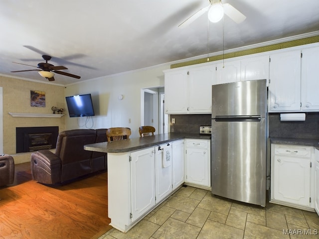 kitchen featuring white cabinetry, kitchen peninsula, stainless steel fridge, crown molding, and decorative backsplash