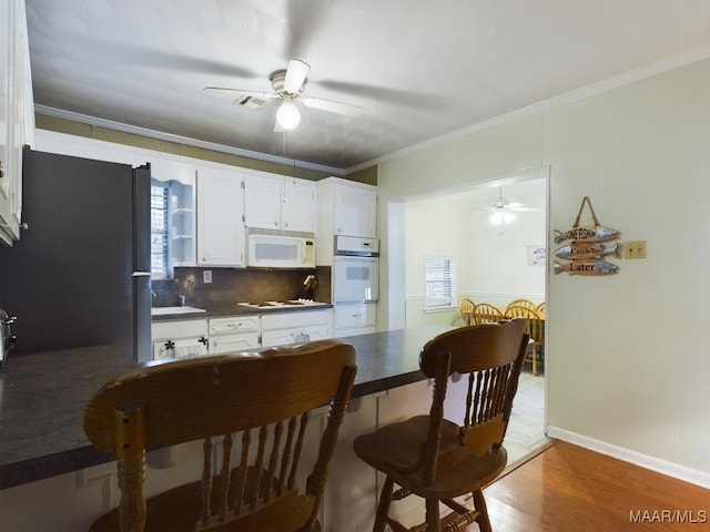 kitchen featuring decorative backsplash, white appliances, crown molding, hardwood / wood-style floors, and white cabinetry