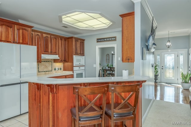 kitchen with kitchen peninsula, a kitchen bar, backsplash, white appliances, and crown molding