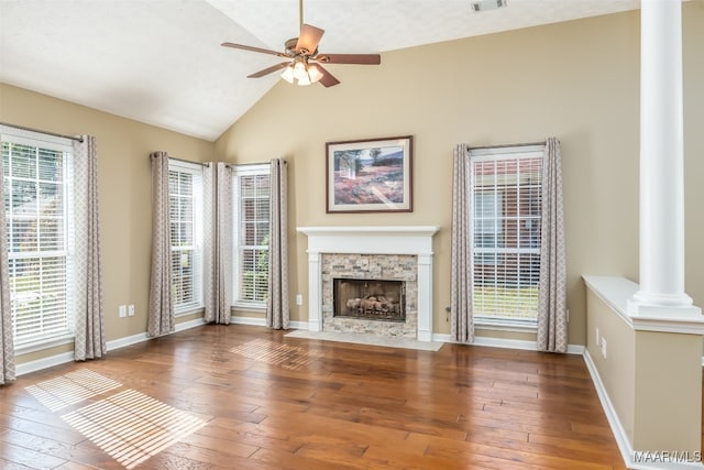 unfurnished living room featuring wood-type flooring, vaulted ceiling, plenty of natural light, and a stone fireplace