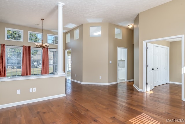 unfurnished room with dark hardwood / wood-style floors, ornate columns, high vaulted ceiling, and an inviting chandelier