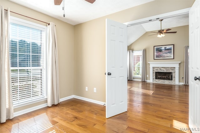 unfurnished living room featuring light hardwood / wood-style floors, vaulted ceiling, a wealth of natural light, and ceiling fan