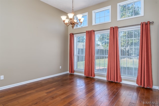 empty room featuring a towering ceiling, dark hardwood / wood-style floors, and a notable chandelier