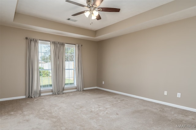 spare room featuring ceiling fan, light colored carpet, and a tray ceiling