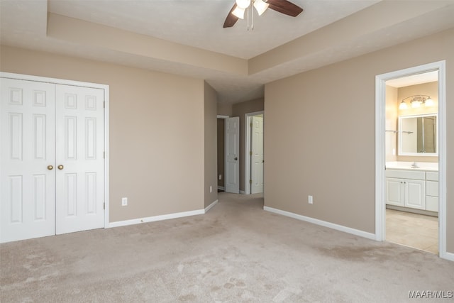 unfurnished bedroom featuring light carpet, sink, ensuite bath, ceiling fan, and a closet