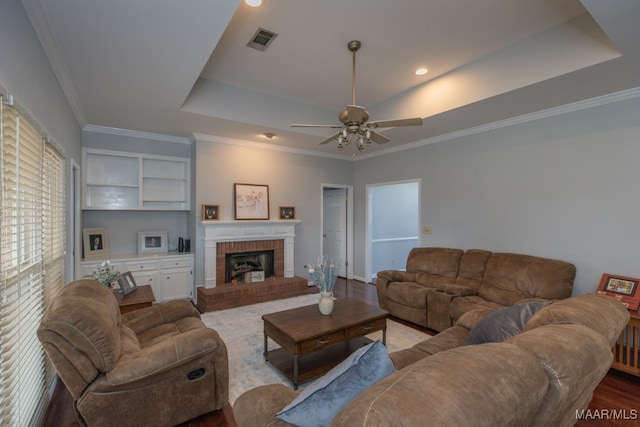 living room with a fireplace, ceiling fan, a raised ceiling, and crown molding