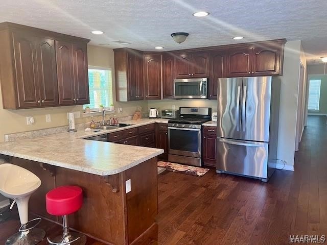 kitchen with sink, dark wood-type flooring, kitchen peninsula, a textured ceiling, and appliances with stainless steel finishes