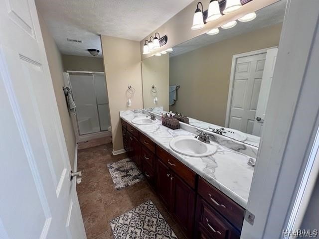 bathroom with a textured ceiling, vanity, and a shower with door