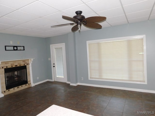 unfurnished living room with a paneled ceiling, ceiling fan, a tile fireplace, and dark tile patterned flooring