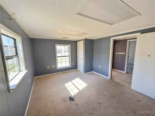 carpeted empty room with a textured ceiling, ornamental molding, attic access, and baseboards