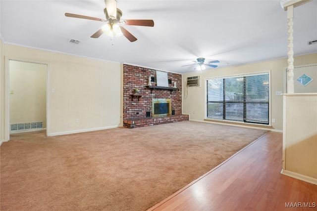 unfurnished living room with a wall unit AC, ceiling fan, crown molding, a fireplace, and light hardwood / wood-style floors