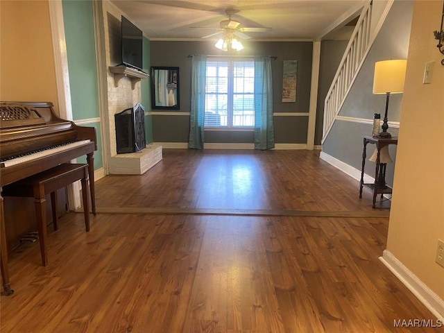 interior space featuring a brick fireplace, hardwood / wood-style flooring, ornamental molding, and ceiling fan