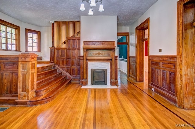 unfurnished living room with an inviting chandelier, a textured ceiling, and light hardwood / wood-style flooring