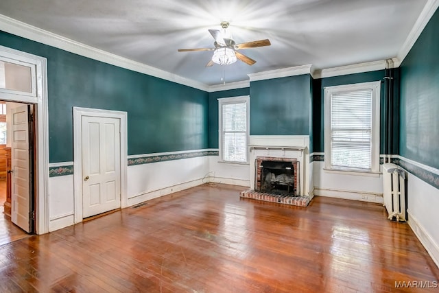 unfurnished living room with wood-type flooring, crown molding, a brick fireplace, ceiling fan, and radiator heating unit