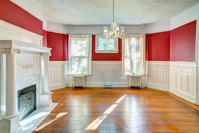 unfurnished dining area featuring radiator, wood-type flooring, a textured ceiling, and an inviting chandelier