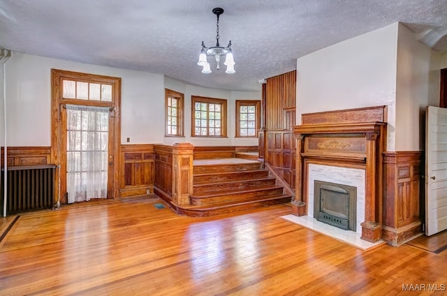 unfurnished living room featuring light hardwood / wood-style flooring, a textured ceiling, and a notable chandelier