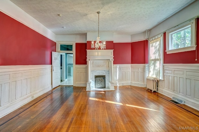 unfurnished living room featuring hardwood / wood-style floors, a textured ceiling, radiator, and a notable chandelier