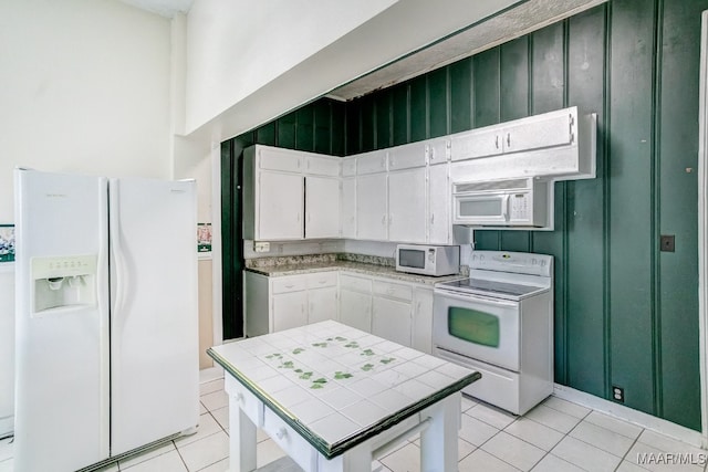 kitchen with tile counters, white cabinets, light tile patterned flooring, and white appliances