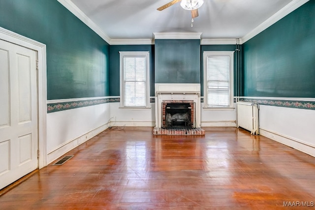 unfurnished living room with radiator, a brick fireplace, ceiling fan, ornamental molding, and wood-type flooring