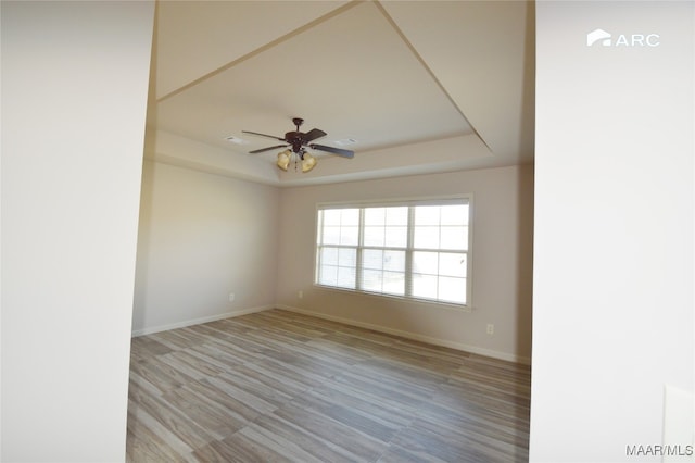 spare room featuring a tray ceiling, ceiling fan, and light wood-type flooring