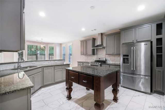 kitchen with appliances with stainless steel finishes, tasteful backsplash, wall chimney exhaust hood, sink, and decorative light fixtures