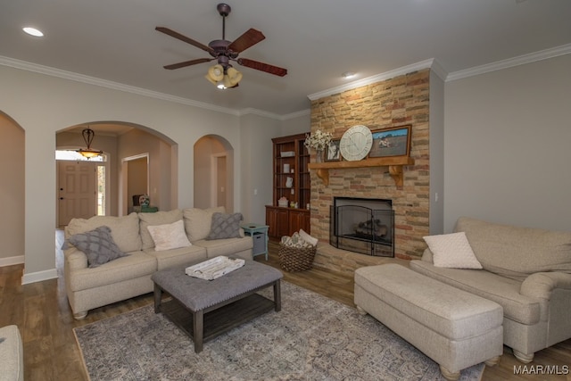 living room featuring a stone fireplace, ceiling fan, dark wood-type flooring, and ornamental molding