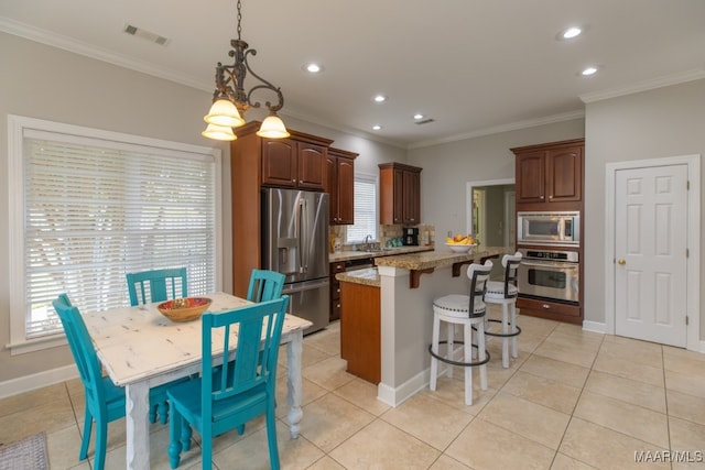 kitchen featuring appliances with stainless steel finishes, ornamental molding, light tile patterned floors, decorative light fixtures, and a kitchen island