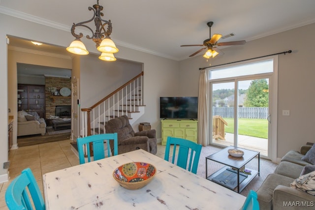 tiled dining space with a fireplace, ceiling fan with notable chandelier, and ornamental molding