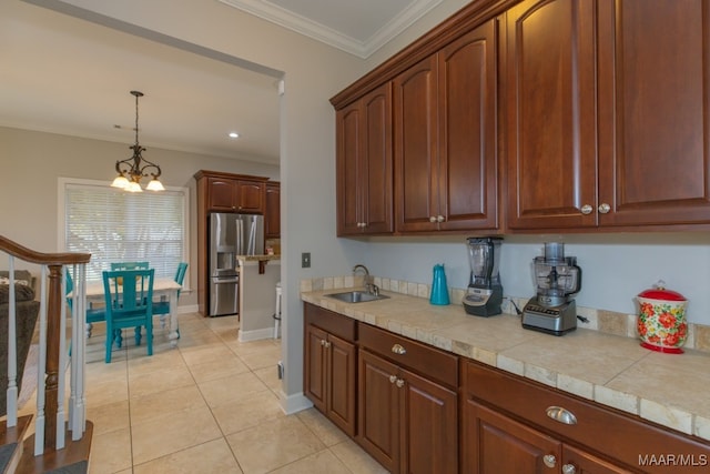 kitchen featuring sink, stainless steel refrigerator with ice dispenser, tile countertops, crown molding, and decorative light fixtures