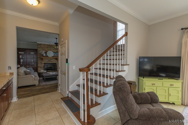 stairway with tile patterned flooring, a stone fireplace, and ornamental molding