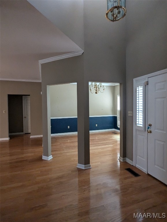 foyer entrance featuring hardwood / wood-style floors, a notable chandelier, ornamental molding, and a high ceiling