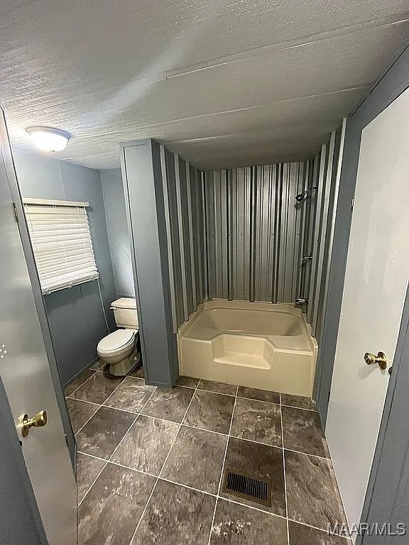 bathroom featuring toilet, shower / bath combination, and a textured ceiling