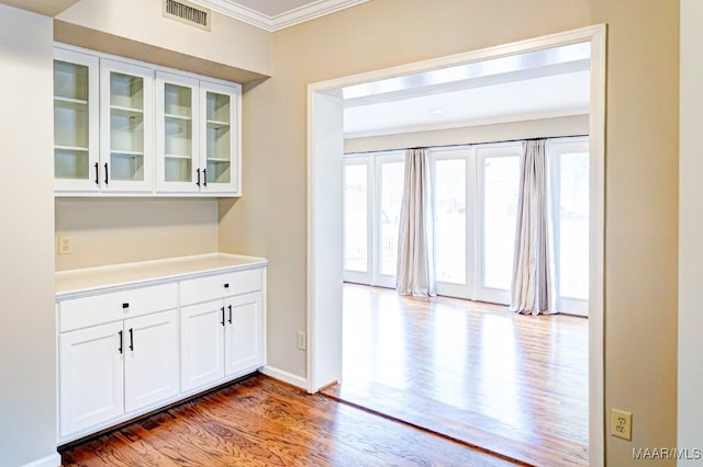 interior space featuring baseboards, visible vents, wood finished floors, and ornamental molding