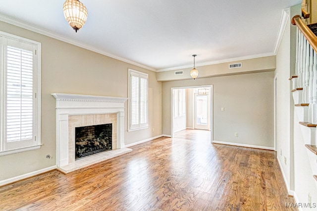 unfurnished living room with crown molding, visible vents, a tiled fireplace, wood finished floors, and stairs