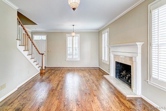 unfurnished living room featuring baseboards, stairway, wood finished floors, and crown molding