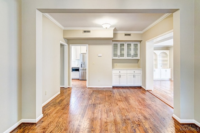 interior space with light wood-type flooring, visible vents, ornamental molding, and baseboards