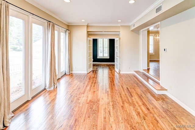 empty room with ornamental molding, light wood-type flooring, visible vents, and baseboards