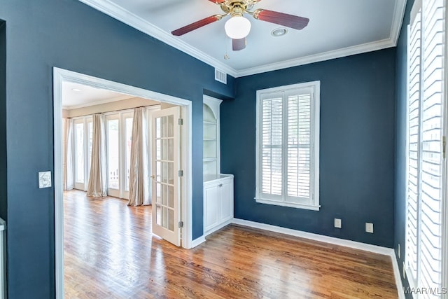 empty room featuring ceiling fan, wood finished floors, visible vents, baseboards, and crown molding