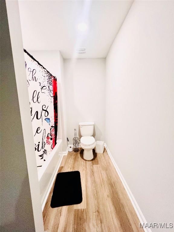 bathroom with wood-type flooring, shower / tub combo with curtain, and toilet