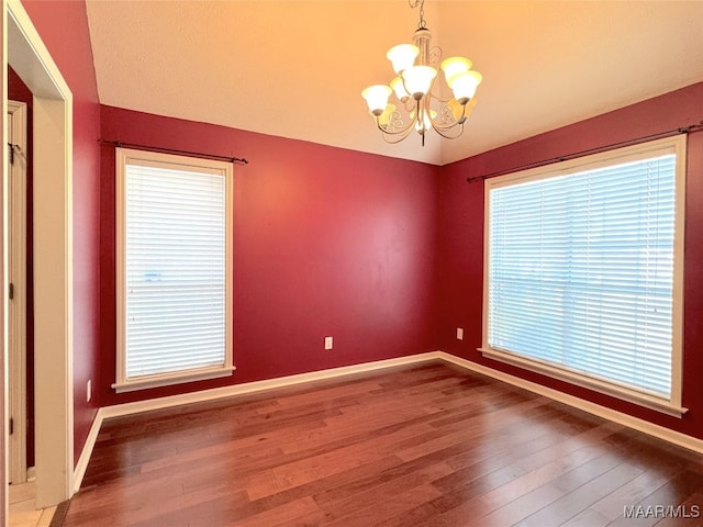 spare room with hardwood / wood-style flooring and an inviting chandelier