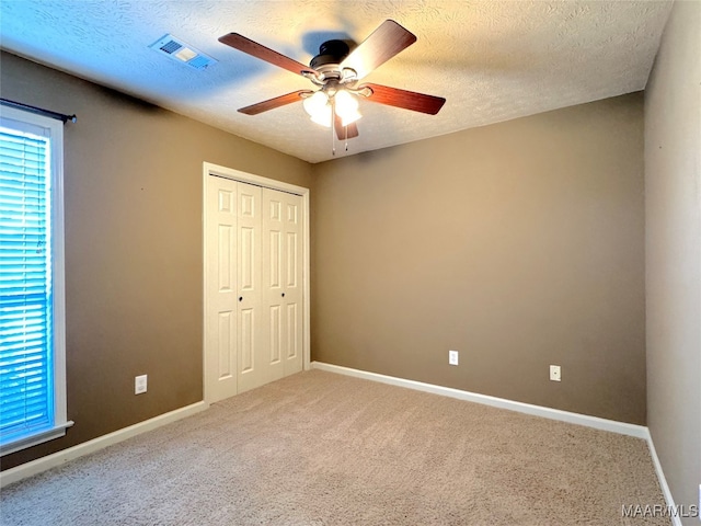 unfurnished bedroom with ceiling fan, carpet flooring, a closet, and a textured ceiling