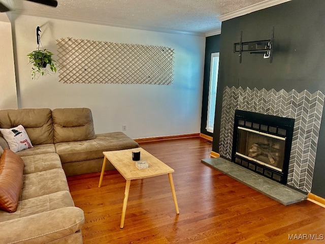 living room featuring a tiled fireplace, crown molding, a textured ceiling, and hardwood / wood-style flooring