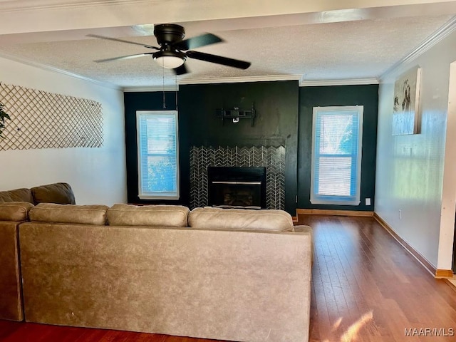 living room with ceiling fan, crown molding, a textured ceiling, a tiled fireplace, and hardwood / wood-style flooring